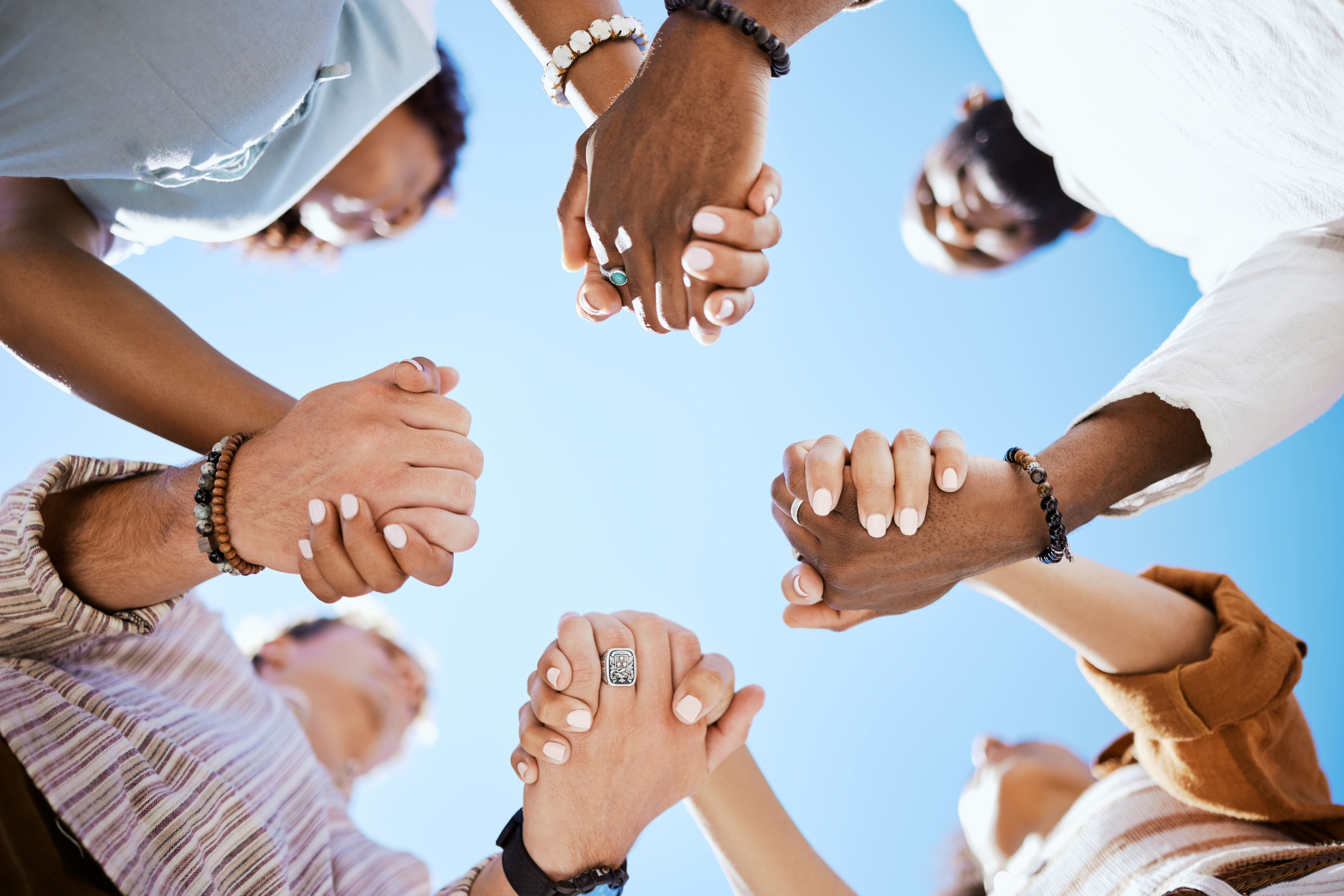 Diversity, support and people holding hands in trust and unity for community against sky background.