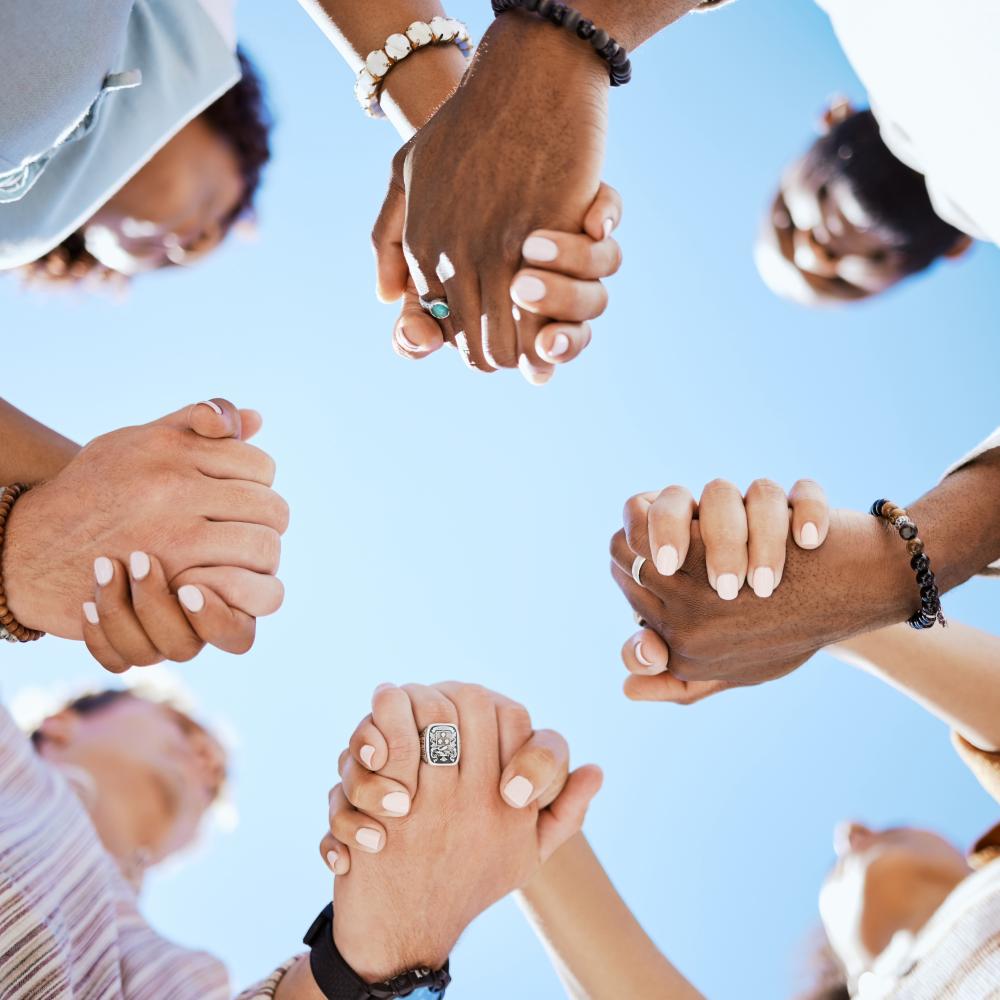 Diversity, support and people holding hands in trust and unity for community against sky background.