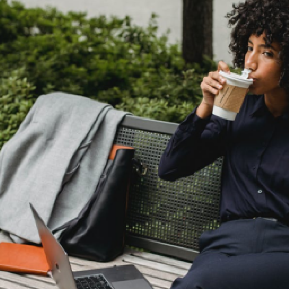 Woman eating and drinking with laptop on bench
